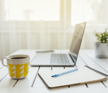 laptop, coffee mug, and notepad on table