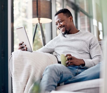 Man looking at ipad while drinking coffee on a couch